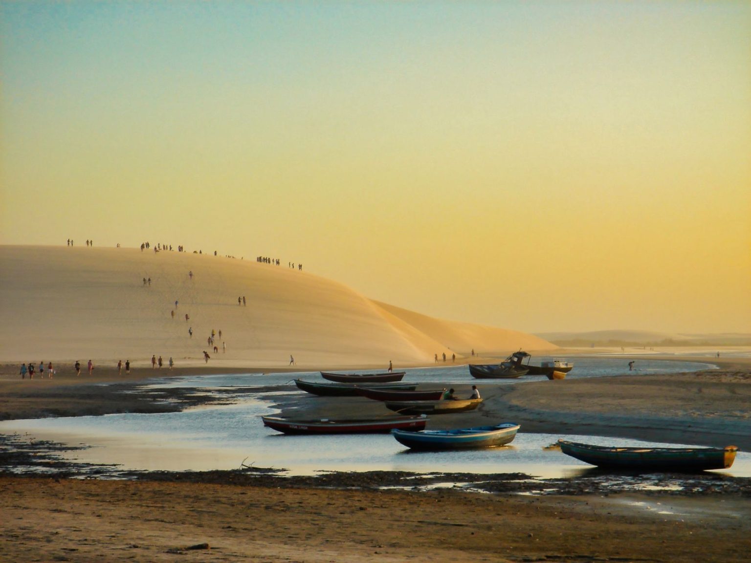 Barcos diante de dunas na praia de Jericoacoara ao pôr do sol