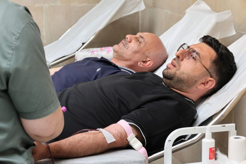 Dois homens doam sangue deitados em leitos hospitalares, acompanhados durante o procedimento de coleta.