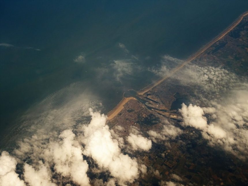 Vista aérea do litoral com áreas de nuvens cobrindo o oceano e a faixa de terra.