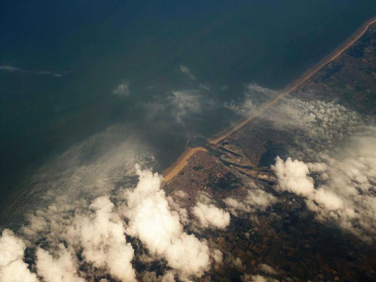 Vista aérea do litoral com áreas de nuvens cobrindo o oceano e a faixa de terra.