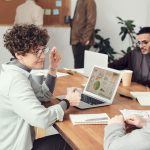 Profissionais reunidos em um escritório analisam dados em um laptop durante uma reunião.