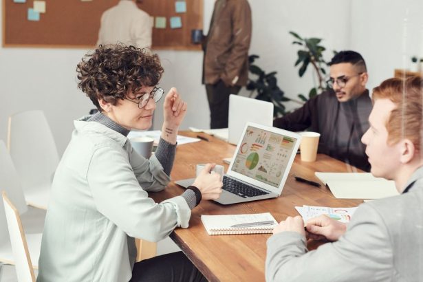 Profissionais reunidos em um escritório analisam dados em um laptop durante uma reunião.