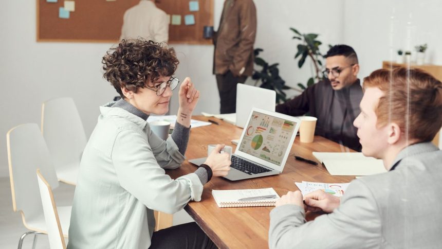 Profissionais reunidos em um escritório analisam dados em um laptop durante uma reunião.