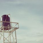 Caixa-d’água industrial instalada sobre uma estrutura metálica contra o céu claro.