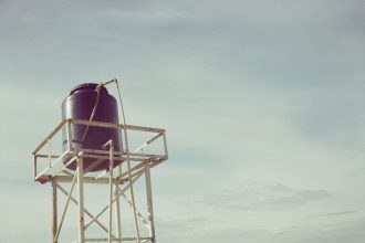 Caixa-d’água industrial instalada sobre uma estrutura metálica contra o céu claro.