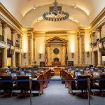 Interior de um plenário legislativo amplo, com colunas, assentos e espaço destinado às atividades parlamentares.