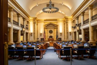Interior de um plenário legislativo amplo, com colunas, assentos e espaço destinado às atividades parlamentares.