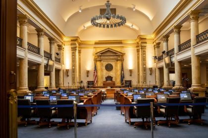 Interior de um plenário legislativo amplo, com colunas, assentos e espaço destinado às atividades parlamentares.